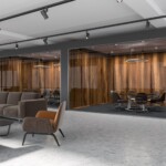 Lobby of a luxury office with dark gray and dark wooden walls, a concrete floor and brown and gray armchairs standing next to gray sofas. A side view. 3d rendering